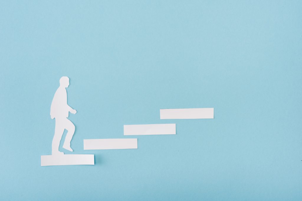 Vista dall'alto dell'uomo di carta sulla scala della carriera sul blu