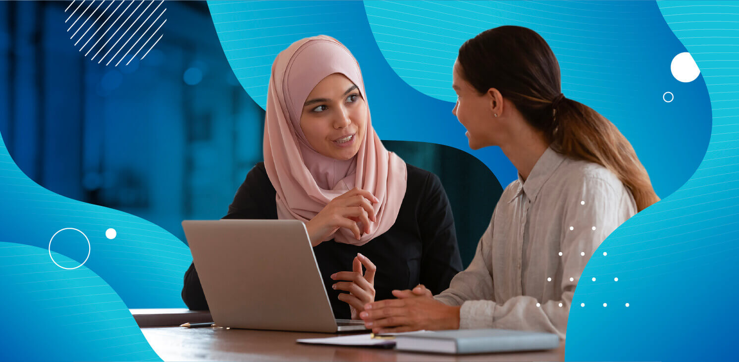 Două femei care vorbesc la un computer cu grafică albastră în jurul lor
