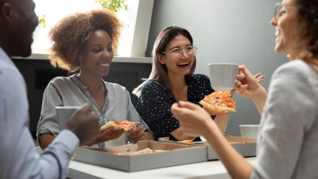 Les employés s'assoient autour d'une table pendant la pause déjeuner et mangent de la pizza ensemble