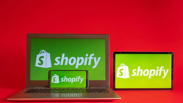 Foto Tokio Japan 05. Juni 2022 Shopify-Webseite wird auf einem modernen Laptop-Smartphone und Notebook auf rotem Hintergrund angezeigt Shopify-Logo auf dem iPhone
