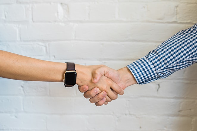 layout di flywheel consigli di LinkedIn per chi cerca lavoro creativo due persone che si stringono la mano con smartwatch e altre con camicia a scacchi