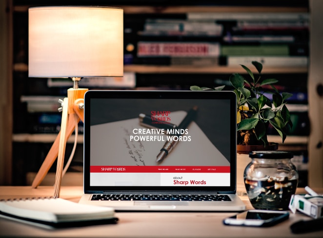 laptop pe birou cu lampă care arată o pagină de pornire a site-ului web pentru o companie numită „Sharp Minds” pe care scrie „Creative Minds Powerful Words”