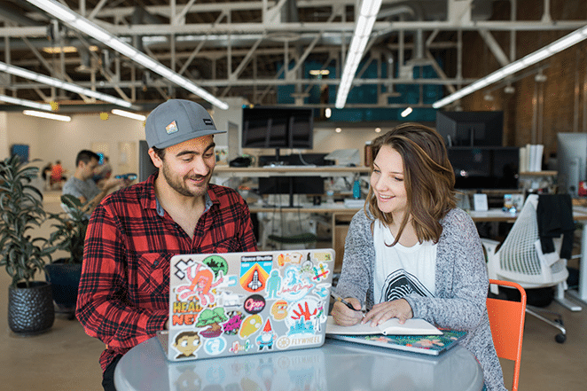 コワーキングスペースでステッカーで覆われたラップトップを持ってテーブルで働く2人のフライウィーラー
