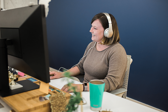 femeie volantă care lucrează pe desktop în fața peretelui marinei ascultând webinar despre testarea utilizatorului