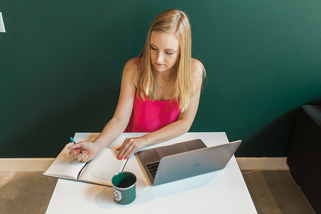 女人在筆記本上寫內容營銷理念,附近有筆記本電腦和飛輪杯