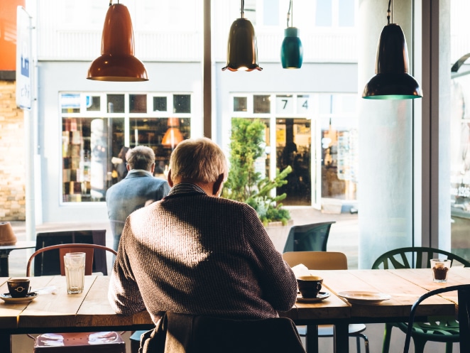 la parte de atrás de la cabeza de dos hombres mientras se sientan en una cafetería frente a una ventana