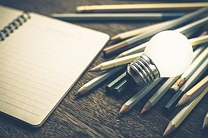 bola lampu yang menyala di atas tumpukan pensil di sebelah notepad untuk menunjukkan bagaimana pemasaran konten memainkan faktor penting dalam strategi SEO Virginia Utara