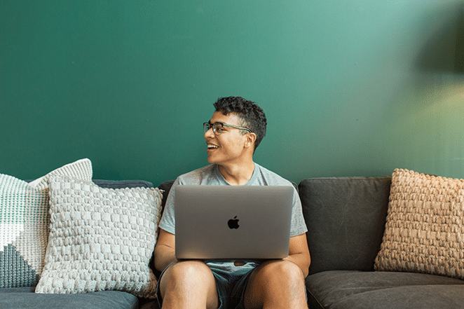 フライホイールによるレイアウトワードプレスが2018年に最高のcmsである理由フォレストグリーンの壁の横にニュートラルな枕が付いた灰色のソファに座っている男性